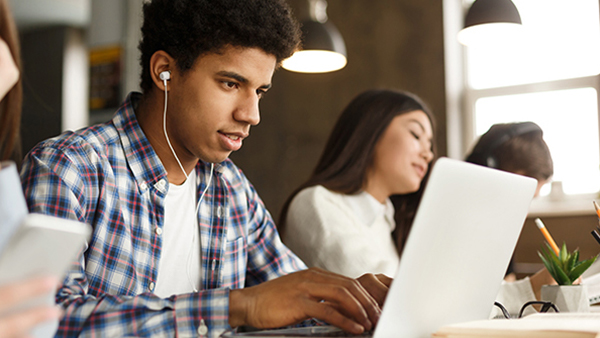 Student wearing earbuds types on laptop