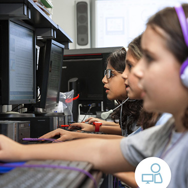 Students in computer lab wear headphones while looking at desktop screens